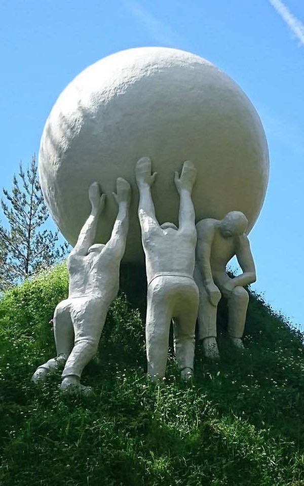 Skulptur, tre menn dytter en ball opp en skråning.